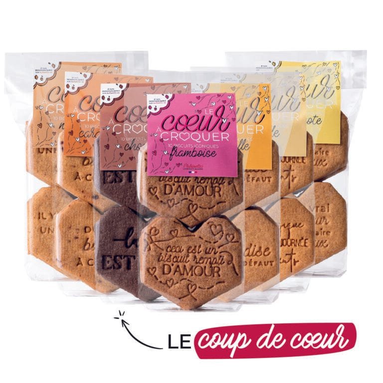 Cinq paquets de cœurs à croquer biscuit personnalisé - le pack, chacun avec une forme de cœur, des étiquettes colorées uniques - dont une variante mirabelle - et le texte français sont affichés ensemble. En dessous, "Le coup de cœur" apparaît avec un soulignement rose et un symbole de cœur.